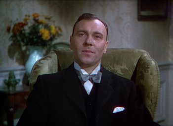 Movie still from “The Four Feathers” (1939), directed by Zoltan Korda – A man sitting in a chair wearing a suit and bow tie; Close Up shot, Low angle