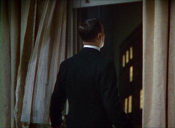 Movie still from “The Four Feathers” (1939), directed by Zoltan Korda – A man in a black suit standing in front of a window; Medium shot, Over the shoulder angle