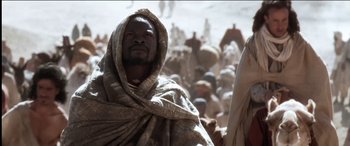 Movie still from “The Four Feathers” (2002), directed by Shekhar Kapur – A man with a beard is wearing a robe and standing in front of a group of people; Medium shot, Low angle