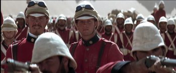 Movie still from “The Four Feathers” (2002), directed by Shekhar Kapur – A man in a red jacket and a helmet is in front of a group of people; Medium shot, Low angle