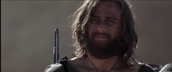 Movie still from “The Four Feathers” (2002), directed by Shekhar Kapur – A man with long hair and a beard holding a rifle; Close Up shot, Over the shoulder angle