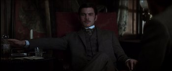 Movie still from “The Four Feathers” (2002), directed by Shekhar Kapur – A man in a suit and tie sitting in a chair; Medium shot, Low angle