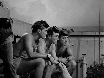 Movie still from “The Frogmen” (1951), directed by Lloyd Bacon – A group of men sitting next to each other on a dock; Medium shot, High angle