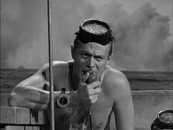 Movie still from “The Frogmen” (1951), directed by Lloyd Bacon – A shirtless man eating a donut while holding a camera; Close Up shot, High angle