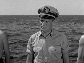 Movie still from “The Frogmen” (1951), directed by Lloyd Bacon – A man wearing a hat standing in front of a body of water; Medium shot, Over the shoulder angle
