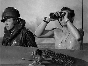 Movie still from “The Frogmen” (1951), directed by Lloyd Bacon – A man is looking through binoculars while another man is sitting in a boat; Medium shot, Over the shoulder angle