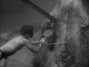 Movie still from “The Frogmen” (1951), directed by Lloyd Bacon – A man holding onto a rope while standing in a pool; Wide shot, High angle