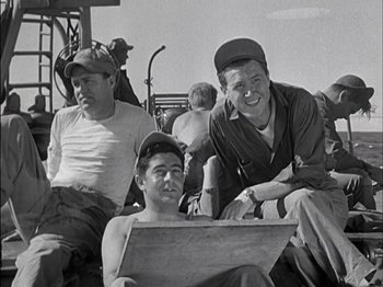 Movie still from “The Frogmen” (1951), directed by Lloyd Bacon – A group of men sitting next to each other on the ground; Medium shot, High angle