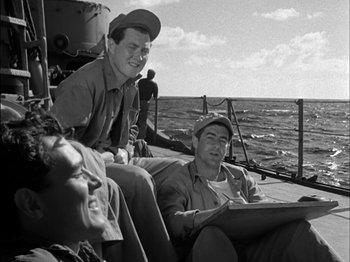 Movie still from “The Frogmen” (1951), directed by Lloyd Bacon – A group of men sitting on top of a boat in the water; Medium shot, Low angle