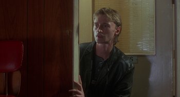 Movie still from “The Full Monty” (1997), directed by Peter Cattaneo – A man in a leather jacket leaning against a door; Medium shot, Over the shoulder angle