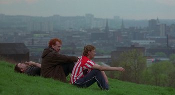 Movie still from “The Full Monty” (1997), directed by Peter Cattaneo – Two men sitting on top of a green hill; Wide shot, High angle