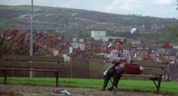 Movie still from “The Full Monty” (1997), directed by Peter Cattaneo – A man sitting on top of a wooden park bench; Wide shot, Low angle