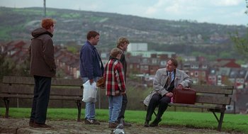 Movie still from “The Full Monty” (1997), directed by Peter Cattaneo – A group of people sitting on a bench in a park; Wide shot, High angle