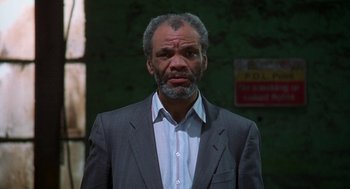 Movie still from “The Full Monty” (1997), directed by Peter Cattaneo – A man in a gray suit and a white shirt; Close Up shot, Low angle