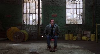 Movie still from “The Full Monty” (1997), directed by Peter Cattaneo – A man sitting on a chair in a room; Wide shot, High angle