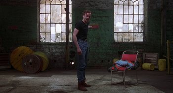 Movie still from “The Full Monty” (1997), directed by Peter Cattaneo – A man standing in an empty room holding a knife; Wide shot, Low angle