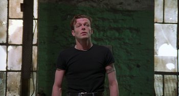 Movie still from “The Full Monty” (1997), directed by Peter Cattaneo – A man in a black t - shirt is looking up; Medium shot, Low angle