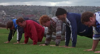 Movie still from “The Full Monty” (1997), directed by Peter Cattaneo – A group of people doing push ups on a field; Wide shot, High angle
