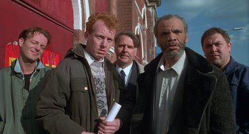 Movie still from “The Full Monty” (1997), directed by Peter Cattaneo – A group of men standing next to each other on a sidewalk; Medium shot, Low angle