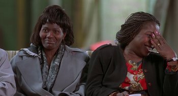 Movie still from “The Full Monty” (1997), directed by Peter Cattaneo – Two women sitting on a couch and one of the women is wearing a wig; Close Up shot, High angle