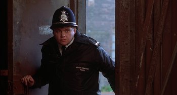 Movie still from “The Full Monty” (1997), directed by Peter Cattaneo – A man in a police uniform standing next to a door; Medium shot, Over the shoulder angle