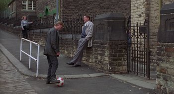 Movie still from “The Full Monty” (1997), directed by Peter Cattaneo – Two men are playing with a soccer ball on the sidewalk; Wide shot, High angle