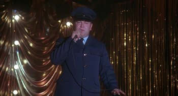 Movie still from “The Full Monty” (1997), directed by Peter Cattaneo – A man in a uniform is singing into a microphone; Medium shot, High angle