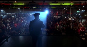 Movie still from “The Full Monty” (1997), directed by Peter Cattaneo – A man standing in front of an audience on a stage; Wide shot, Low angle
