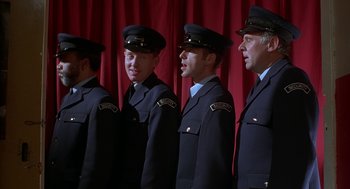 Movie still from “The Full Monty” (1997), directed by Peter Cattaneo – A group of men standing next to each other in uniforms; Medium shot, Low angle