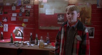 Movie still from “The Full Monty” (1997), directed by Peter Cattaneo – A boy standing in front of a bunch of alcohol bottles; Medium shot, Over the shoulder angle