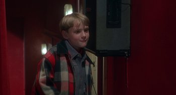 Movie still from “The Full Monty” (1997), directed by Peter Cattaneo – A young boy in a plaid jacket standing next to an electrical box; Medium shot, Over the shoulder angle