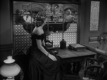 Movie still from “The Furies” (1950), directed by Anthony Mann – A woman in a black dress sitting at a table; Medium shot, Over the shoulder angle