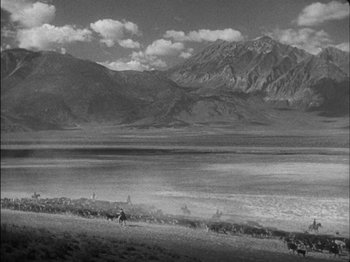 Movie still from “The Furies” (1950), directed by Anthony Mann – A black and white photo of mountains and a lake; Extreme Wide shot, High angle