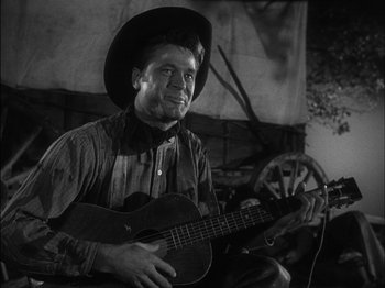 Movie still from “The Furies” (1950), directed by Anthony Mann – A man wearing a cowboy hat playing a guitar; Close Up shot, Low angle