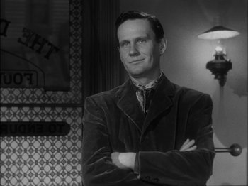Movie still from “The Furies” (1950), directed by Anthony Mann – A man standing with his arms crossed in front of a lamp; Close Up shot, Over the shoulder angle