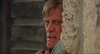 Movie still from “The Fury” (1978), directed by Brian De Palma – An older man is looking at the camera while standing next to a stone wall; Close Up shot, Low angle