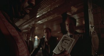 Movie still from “The Fury” (1978), directed by Brian De Palma – A man holding a photo of himself in a crowd; Close Up shot, Over the shoulder angle