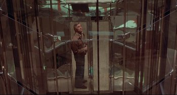 Movie still from “The Fury” (1978), directed by Brian De Palma – A man standing in front of a glass door; Wide shot, Low angle
