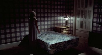 Movie still from “The Fury” (1978), directed by Brian De Palma – A woman standing on a bed in a room with a lamp; Wide shot, High angle