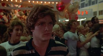 Movie still from “The Fury” (1978), directed by Brian De Palma – A young man in striped shirt in a crowd of people; Close Up shot, Over the shoulder angle