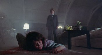Movie still from “The Fury” (1978), directed by Brian De Palma – A woman laying on the ground in a room with a man standing in the background; Wide shot, Low angle