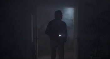 Movie still from “The Fury” (1978), directed by Brian De Palma – A man standing in a doorway holding a flashlight; Wide shot, Low angle