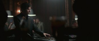 Movie still from “The Gambler” (2014), directed by Rupert Wyatt – A man sitting at a table in a room; Medium shot, Over the shoulder angle