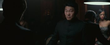 Movie still from “The Gambler” (2014), directed by Rupert Wyatt – A man in a black suit is sitting in a chair; Medium shot, Over the shoulder angle