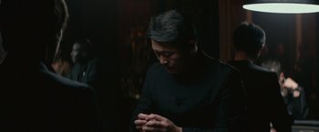 Movie still from “The Gambler” (2014), directed by Rupert Wyatt – A man in a black shirt is looking down at his hands; Medium shot, Over the shoulder angle