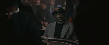 Movie still from “The Gambler” (2014), directed by Rupert Wyatt – A man sitting at a table in front of a group of people; Close Up shot, Over the shoulder angle