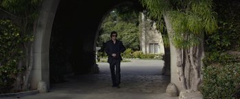 Movie still from “The Gambler” (2014), directed by Rupert Wyatt – A man wearing a suit and sunglasses walking through an archway; Wide shot, Low angle
