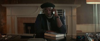 Movie still from “The Gambler” (2014), directed by Rupert Wyatt – A man sitting at a table with a stack of books on top of it; Close Up shot, High angle