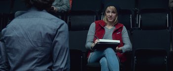 Movie still from “The Gambler” (2014), directed by Rupert Wyatt – A woman sitting in a chair with a book in her lap; Medium shot, Over the shoulder angle