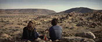 Movie still from “The Gambler” (2014), directed by Rupert Wyatt – Two people sitting on a rock in the desert; Wide shot, Over the shoulder angle